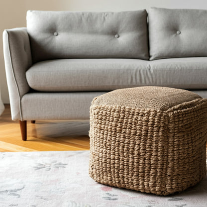 Brown woven ottoman in front of a gray sofa in a living room setting.