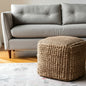 Brown woven ottoman in front of a gray sofa in a living room setting.
